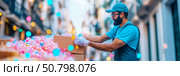 Volunteer Packing Colorful Treats in City Setting: man in blue shirt and cap carefully packs colorful treats into boxes amidst festive city street scene. Стоковое AI-изображение, AI-художник Данила Большаков / Фотобанк Лори