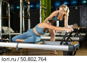 Girl trainer helps young woman to perform exercises in sitting position on pilates reformer. Стоковое фото, фотограф Яков Филимонов / Фотобанк Лори