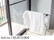 Folding drying rack with hanging white towel in a room with a large window and a balcony. Interior and amenities. Стоковое фото, фотограф Коханова Наталья / Фотобанк Лори