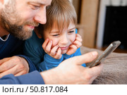 Father and son little boy laughing and using phone. They watching funny videos together, playing games on smartphone. Concept technology, smart phone addicted. Fun weekend activity. Modern fatherhood. Стоковое фото, фотограф Марина Демидюк / Фотобанк Лори