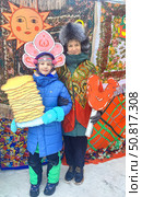 Женщина с петушком и ребенок с блинами позируют на масленицу. A woman with a cockerel and a child with pancakes pose on Shrovetide. (2024 год). Редакционное фото, фотограф Денис Баданин / Фотобанк Лори