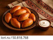 Пирожки. Пирожки на тарелке с узором, рядом миска со сметаной. Стоковое AI-изображение, AI-художник Башкирова Анна / Фотобанк Лори