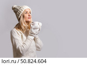 Woman in warm woolen white sweater, cap with bubo and mittens holds cup, smiles and looks up dreamily. Стоковое фото, фотограф Екатерина Красникова / Фотобанк Лори