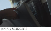 Airplane passenger opens and unfolds folding tray table in front seat by window, preparing for meal or work during daylight flight, close up of hands and aircraft interior, sky outside window view. Стоковое видео, видеограф Сергей Тимофеев / Фотобанк Лори