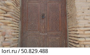 Antique wooden carved door with intricate oriental floral patterns set in sunlit yellow brick wall, historical architecture detail with traditional craftsmanship and aged surface texture from Asia. Редакционное видео, видеограф Сергей Тимофеев / Фотобанк Лори