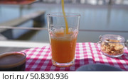 Pouring orange juice into glass on checkered tablecloth near lake. Стоковое видео, видеограф Данил Руденко / Фотобанк Лори