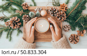 Winter Warmth: A hand holding a candle centerpiece with evergreen sprigs, pinecone and wooden tray. Стоковое AI-изображение, AI-художник Данила Большаков / Фотобанк Лори