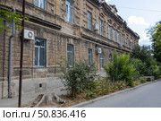 Yevpatoria, Russian Federation - July 05, 2025: Historic stone building with air conditioning units and overgrown greenery along the street, showcasing urban architecture and nature's encroachment. Редакционное фото, фотограф Ирина Ручушкина / Фотобанк Лори