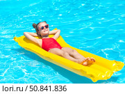 Happy little girl in red swimsuit lies comfortably on yellow inflatable mattress in swimming pool with blue water on warm summer day on tropical vacation. Relaxation, fun, carefree childhood concept. Стоковое фото, фотограф Ирина Михайличенко / Фотобанк Лори