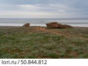 Fancy stones on the slopes of Bolshoe Bogdo Mountain and the salt lake Baskunchak in the distance on a summer day, Bogdinsko-Baskunchak Nature Reserve, Akhtubinsky district, Astrakhan region, Russia. Стоковое фото, фотограф Ula Ulachka / Фотобанк Лори