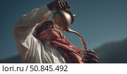 Traditional Arab man pouring tea from brass dallah outdoors in sunlight. Стоковое AI-изображение, AI-художник Катерина Бондарец / Фотобанк Лори