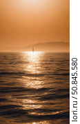 Sailboat gliding on calm sea at golden sunset with warm light, tranquil water, and serene mountain silhouette in the distance. Стоковое AI-изображение, AI-художник Катерина Бондарец / Фотобанк Лори