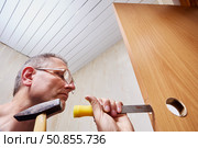 Carving mortise in wooden door, repairman uses chisel and hammer to carefully shape hole for lock installation during door hardware fitting process. Стоковое фото, фотограф Владимир Григорьев / Фотобанк Лори