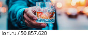Celebratory moment: Hand offering glass of amber liquor on ice, evoking warmth and conviviality, for use in restaurant promotion. Стоковое AI-изображение, AI-художник Данила Большаков / Фотобанк Лори