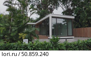 Minimalist rental dwelling nestled within verdant tropical landscape, surrounded by palm trees, providing serene and secluded living environment. Стоковое AI-видео, аниматор Данил Руденко / Фотобанк Лори