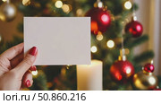 Christmas blank card in Female hand. White greeting card among decorated Christmas tree with holiday decorations. Frame note mock up with space for text. Empty paper sheet. Seasons greetings. Template. Стоковое AI-видео, аниматор Марина Демидюк / Фотобанк Лори