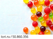 Bright glossy jelly candies in various colors placed on light wooden surface, representing sweet treats and confectionery concept. Стоковое AI-изображение, AI-художник Александра Рублева / Фотобанк Лори