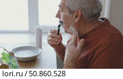Senior Man shaving his face. Old male shaves beard and mustache with shaver. Elderly gray haired man looking at the mirror, applies shaving cream foam and using razor. Skin hygiene. Daily body care. Стоковое видео, видеограф Марина Демидюк / Фотобанк Лори