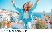 Joyful Exuberance: A woman's spirited celebration against a picturesque coastal town, for personal blog or lifestyle content. Стоковое AI-изображение, AI-художник Данила Большаков / Фотобанк Лори