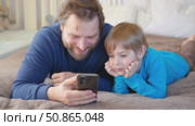 Father and son little boy laughing and using phone. They watching funny videos together, playing games on smartphone. Concept technology, smartphone addicted. Fun weekend activity. Modern fatherhood. Стоковое видео, видеограф Марина Демидюк / Фотобанк Лори