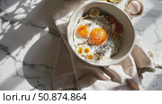 Delicious and healthy breakfast with fried eggs, sesame seeds, daisies, and vegetables served in a bowl on a marble table with natural light creating shadows. Стоковое AI-видео, аниматор Данил Руденко / Фотобанк Лори