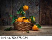 Large ripe tangerines with green leaves lie in a wicker basket on a wooden tabletop. Selective focus. Стоковое фото, фотограф Анищенко Геннадий / Фотобанк Лори