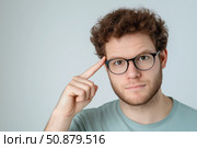 Serious young man in eyeglasses looking at camera and points his finger to his temple. Стоковое AI-изображение, AI-художник Евгений Харитонов / Фотобанк Лори