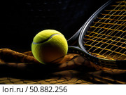 Tennis ball and racket resting on netting in dramatic lighting. Стоковое AI-изображение, AI-художник Иван Рябоконь / Фотобанк Лори