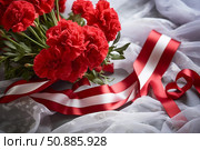 Red carnations with red and white ribbon celebrating national holiday. Стоковое AI-изображение, AI-художник Иван Рябоконь / Фотобанк Лори