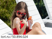 Sun protection. Cute little girl applied sunscreen to her tanned shoulder in the shape of a sun. Skin care. Child sitting on sunbed, sunbathing near hotel pool. High quality photo. Summer vacation. Стоковое фото, фотограф Ирина Михайличенко / Фотобанк Лори
