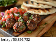 Delicious grilled kofta kebabs served with pita bread and tomato salad. Стоковое AI-изображение, AI-художник Иван Рябоконь / Фотобанк Лори