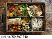 Metal lunchbox full of tasty sandwiches, vegetables, and bread on rustic wooden table. Стоковое AI-изображение, AI-художник Иван Рябоконь / Фотобанк Лори