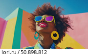 Radiant individual with curly hair and vibrant sunglasses expressing joy against a colorful geometric wall under a clear sky. Стоковое AI-видео, аниматор Данила Большаков / Фотобанк Лори