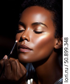 Makeup artist applying highlighter to model's cheek at a beauty studio during evening session. Стоковое AI-изображение, AI-художник Сергей Толмачёв / Фотобанк Лори