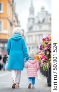 Generational bond: Grandmother and granddaughter stroll through a vibrant city street, hand in hand. Стоковое AI-изображение, AI-художник Данила Большаков / Фотобанк Лори