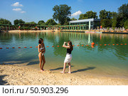 Красивые девушки фотографируются в купальниках на фоне воды./ Pioneer Pond. Beach recreation on the water near the pond in Gorky Park, Moscow, 2025. Beautiful girls are photographed in bathing suits against the backdrop of water. Редакционное фото, фотограф Iva Noel / Фотобанк Лори