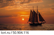 A sailboat glides across the ocean waters as the sun sets, casting a warm glow on the horizon. Стоковое AI-изображение, AI-художник Данила Большаков / Фотобанк Лори