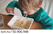 6 years old boy eats instant noodle from box. Child is eating spaghetti. Lunch time. A good appetite. Tasty children food. Close-up portrait. Carbs dinner. Fast food. Kid eating by himself with fork. Стоковое видео, видеограф Марина Демидюк / Фотобанк Лори