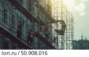 A group of construction workers on scaffolding near the facade of a building. People in hard hats and safety vests are busy assembling or repairing the structure. The scene is shot against the backdrop of the morning or evening sky, creating a contrast with the metal elements of the scaffolding. The image conveys the dynamics of labor, architectural details and the theme of industrial development. Suitable for illustrating themes of safety, construction, repair and urbanism. Стоковое AI-изображение, AI-художник Анна Кривицкая / Фотобанк Лори