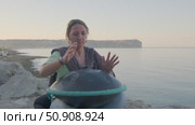On the seashore, a woman plays a musical instrument handpan or hang. Стоковое видео, видеограф Boris Vasilenko / Фотобанк Лори