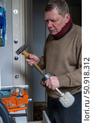 Senior man engrossed in home improvement project using hammer and toilet brush for inventive solution. Стоковое фото, фотограф Данила Большаков / Фотобанк Лори