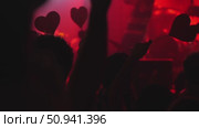 Crowd of concertgoers holding heart-shaped signs in vibrant red lighting atmosphere. Стоковое видео, видеограф Данил Руденко / Фотобанк Лори