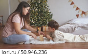 Happy mom and little child boy sit on a floor near Xmas tree, play board game with wooden tower together at home while spending leisure time at cozy home during Christmas holidays. Indoor activities. Стоковое видео, видеограф Ирина Михайличенко / Фотобанк Лори
