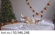 Two cute charming little sibling children having fun at home, jumping on a bed in a sunlit cozy bedroom with New Year and Christmas tree and gifts background. Slow motion winter holidays footage. Стоковое видео, видеограф Ирина Михайличенко / Фотобанк Лори