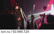 Crowd of concertgoers holding red heart-shaped signs under vibrant stage lights. Стоковое видео, видеограф Данил Руденко / Фотобанк Лори