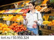 Woman carefully selects fresh tomatoes, standing near the counter in supermarket. Стоковое фото, фотограф Яков Филимонов / Фотобанк Лори