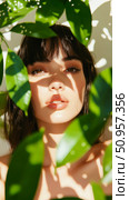 Close-up portrait of a serene woman's face, beautifully framed by vibrant green foliage and dappled sunlight, a celebration of natural connection. Стоковое AI-изображение, AI-художник Данила Большаков / Фотобанк Лори