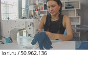 A young seamstress at a craft denim store is embroidering thick gloves for hands made from denim fabric. Стоковое видео, видеограф Strunov David / Фотобанк Лори