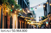 Festive outdoor string light illumination, decorating old buildings for a street party atmosphere. Стоковое AI-изображение, AI-художник Данила Большаков / Фотобанк Лори