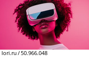 Technological immersion: woman wearing virtual reality headset against pink colored plain backdrop, augmented reality interface, futuristic experience. Стоковое AI-изображение, AI-художник Данила Большаков / Фотобанк Лори